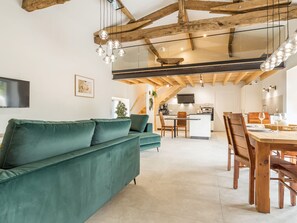 A modern interior with a green sofa, wooden dining table, and kitchen area. - Renovated cottage in serene countryside (Saint-Père-en-Retz)