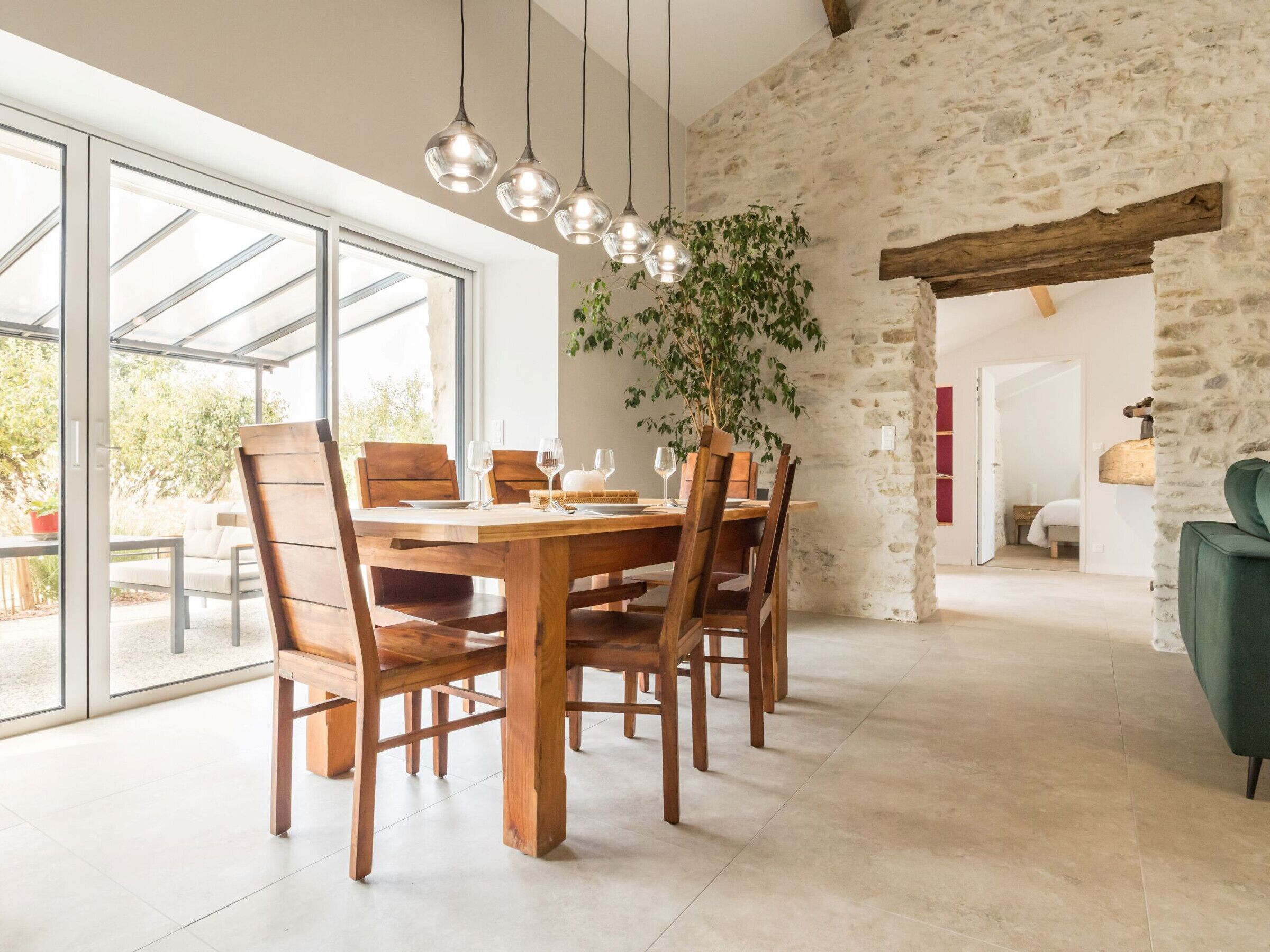 A dining area with a wooden table and chairs, a hanging light fixture, and a potted plant.