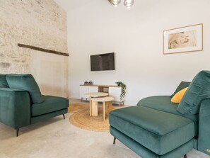 A modern living room with two green sofas, a small wooden table, a TV mounted on the wall, and a framed picture. - Renovated cottage in serene countryside (Saint-Père-en-Retz)