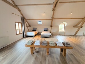 A loft bedroom with two beds, a wooden table with towels, and skylights.