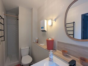 A bathroom with a toilet, a shower, a sink, a mirror, and a towel rack.