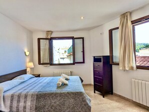 A bedroom with a bed, a dresser, a radiator, a window with curtains, and a wall-mounted mirror. - Historic duplex with sea views - 6 guests (Tossa de Mar)