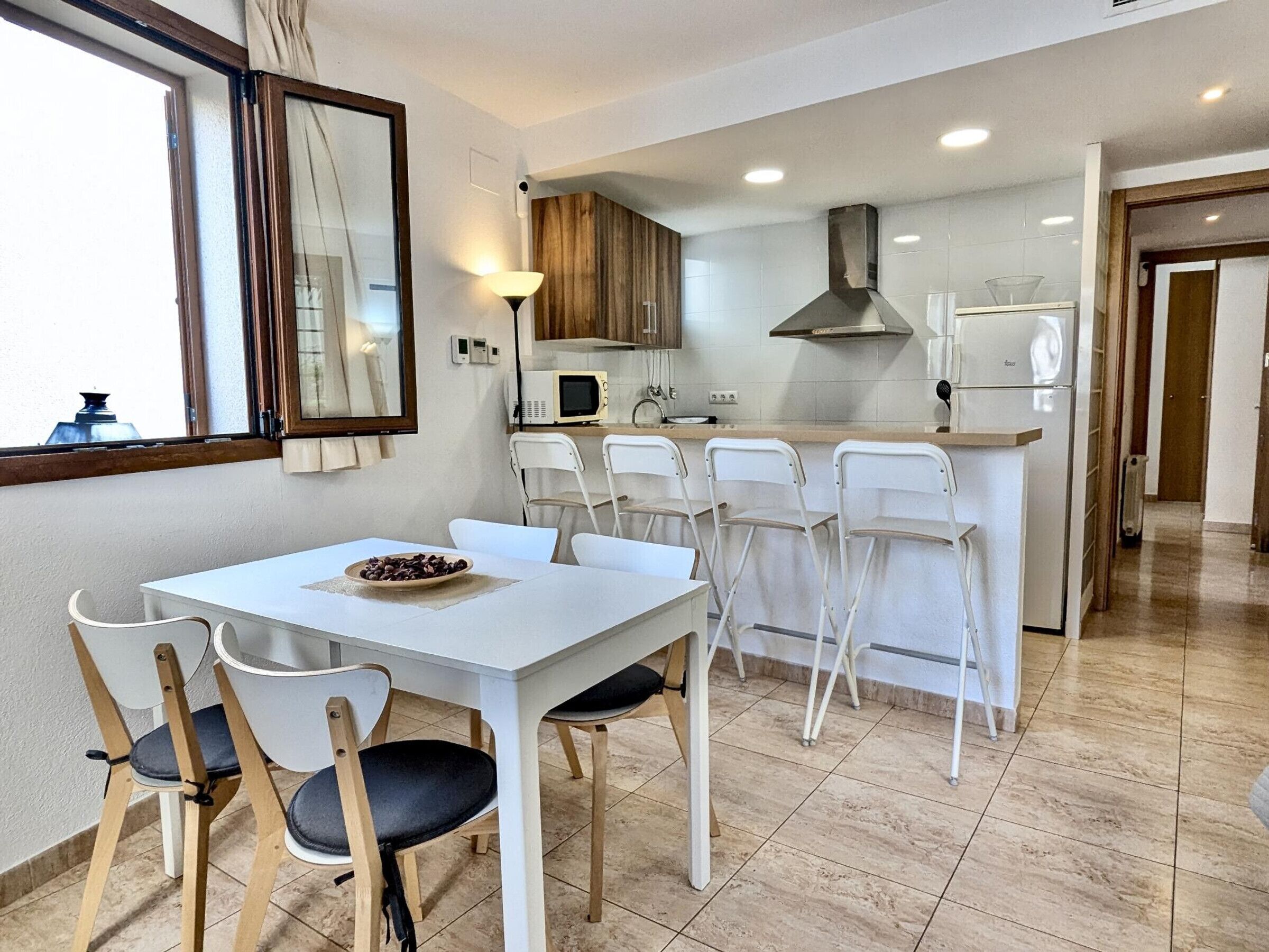 A modern kitchen with white cabinetry, a central island, and a dining area with a white table and chairs.