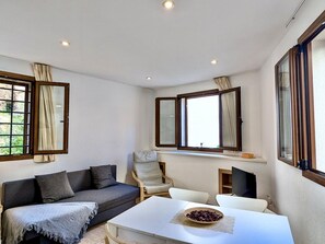 Ein modernes Wohnzimmer mit einer Couch, einem Esstisch und zwei mit Vorhängen versehenen Fenstern.