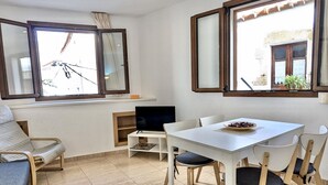 Una habitación con una mesa blanca, sillas, un televisor y una ventana con cortinas.