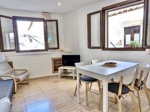 Ein Zimmer mit einem weißen Tisch, Stühlen, einem Fernseher und einem Fenster mit Vorhängen.