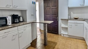 Eine Küche mit weißen Schränken, einer Granit Arbeitsplatte, einer Mikrowelle, einer Kaffeemaschine und einer Holztür.