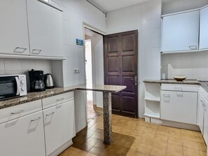 Eine Küche mit weißen Schränken, einer Granit Arbeitsplatte, einer Mikrowelle, einer Kaffeemaschine und einer Holztür.