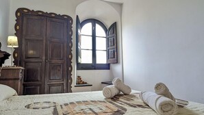 Ein Zimmer mit einem Bett, einem Holzschrank, einem kleinen Tisch mit einer Lampe und einem Fenster mit Blick.