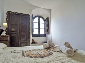 Ein Zimmer mit einem Bett, einem Holzschrank, einem kleinen Tisch mit einer Lampe und einem Fenster mit Blick.
