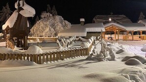 A snow-covered outdoor area with a wooden fence, a wooden structure with a roof, and a building with a covered porch. - Charming apartment at the foot of the slopes - 5 guests (Crest-Voland)