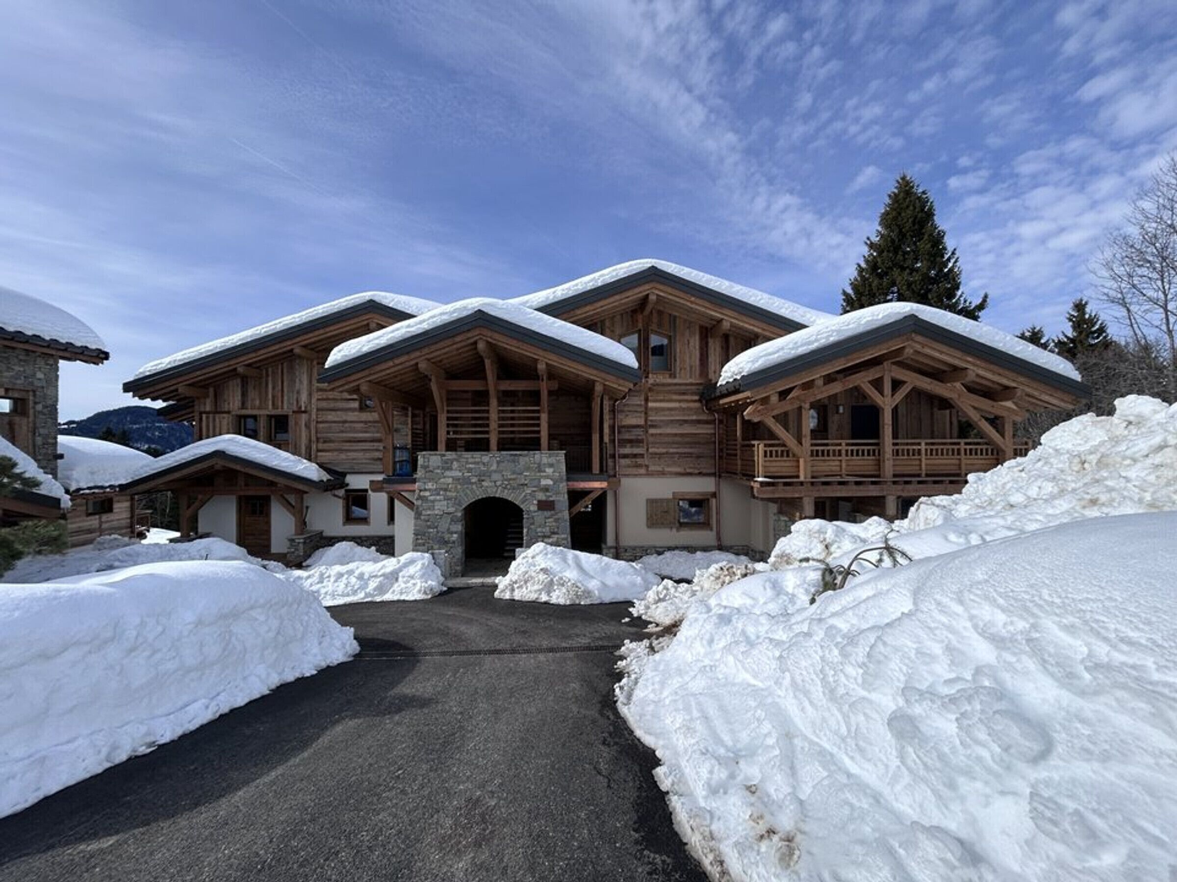 Un grand chalet en bois, doté d’une entrée en pierre et entouré de neige.