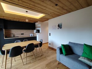 Une cuisine moderne avec un plafond en bois, une table à manger avec des chaises et un canapé gris agrémenté de coussins verts.