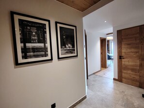 Un couloir avec deux photographies en noir et blanc encadrées accrochées au mur, une porte en bois et un sol carrelé.