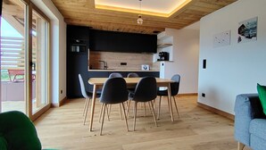A modern interior with a wooden ceiling, a dining area with chairs, a kitchen with a black countertop, and a view through a glass door. - Charming apartment at the foot of the slopes - 5 guests (Crest-Voland)