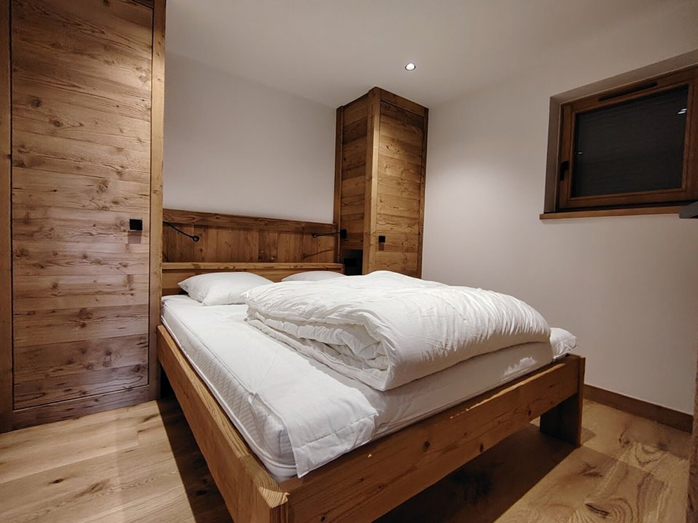 A bedroom with a wooden bed frame, a headboard, and a window.