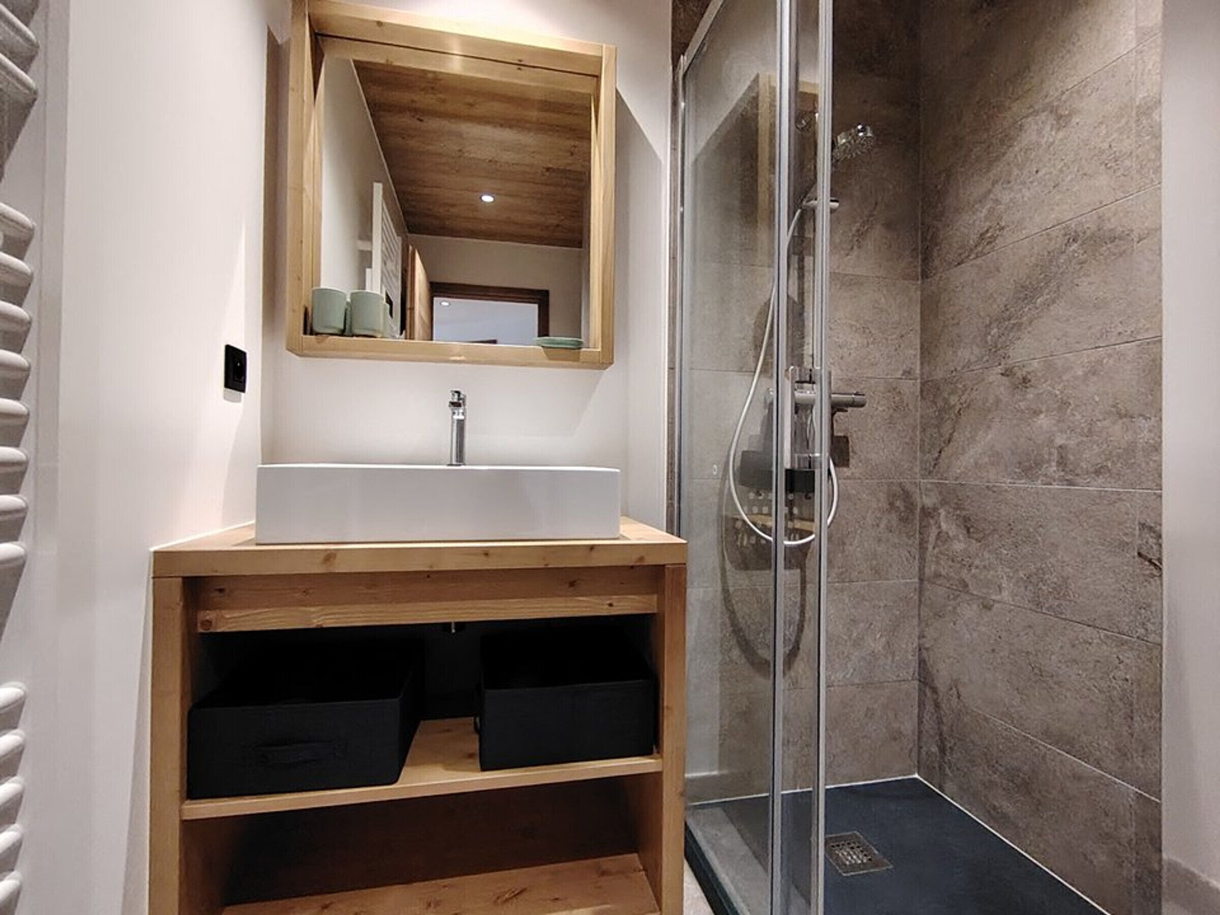 Une salle de bain avec un meuble-lavabo en bois, un miroir, un lavabo et une douche à parois de verre.