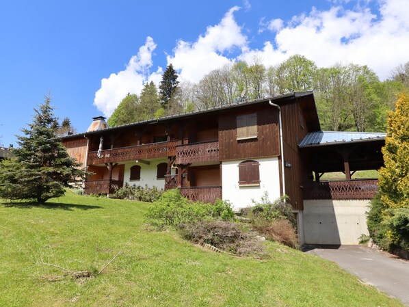 Ein traditionelles Holzchalet mit Balkon, umgeben von einem gepflegten Garten und Bäumen.