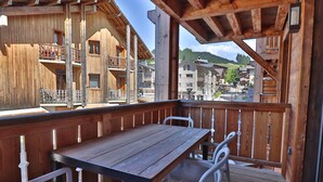 A wooden deck with a table and chairs, overlooking a mountainous area with buildings. - Modern apartment, elevator - 6 guests (Les Gets)