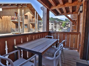 A wooden deck with a table and chairs, overlooking a mountainous area with buildings. - Modern apartment, elevator - 6 guests (Les Gets)
