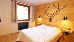 A bedroom with a large bed, a window with curtains, a wall-mounted tree design, and bedside lamps. - Modern apartment, elevator - 6 guests (Les Gets)