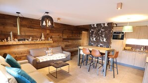 A modern living space with a sofa, coffee table, and a dining area with chairs. There is a kitchen with a stove and cabinets. - Modern apartment, elevator - 6 guests (Les Gets)