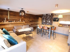 A modern living space with a sofa, coffee table, and a dining area with chairs. There is a kitchen with a stove and cabinets. - Modern apartment, elevator - 6 guests (Les Gets)