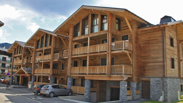 A multi-story wooden building with balconies, a stone base, and a street in front. - Modern apartment, elevator - 6 guests (Les Gets)