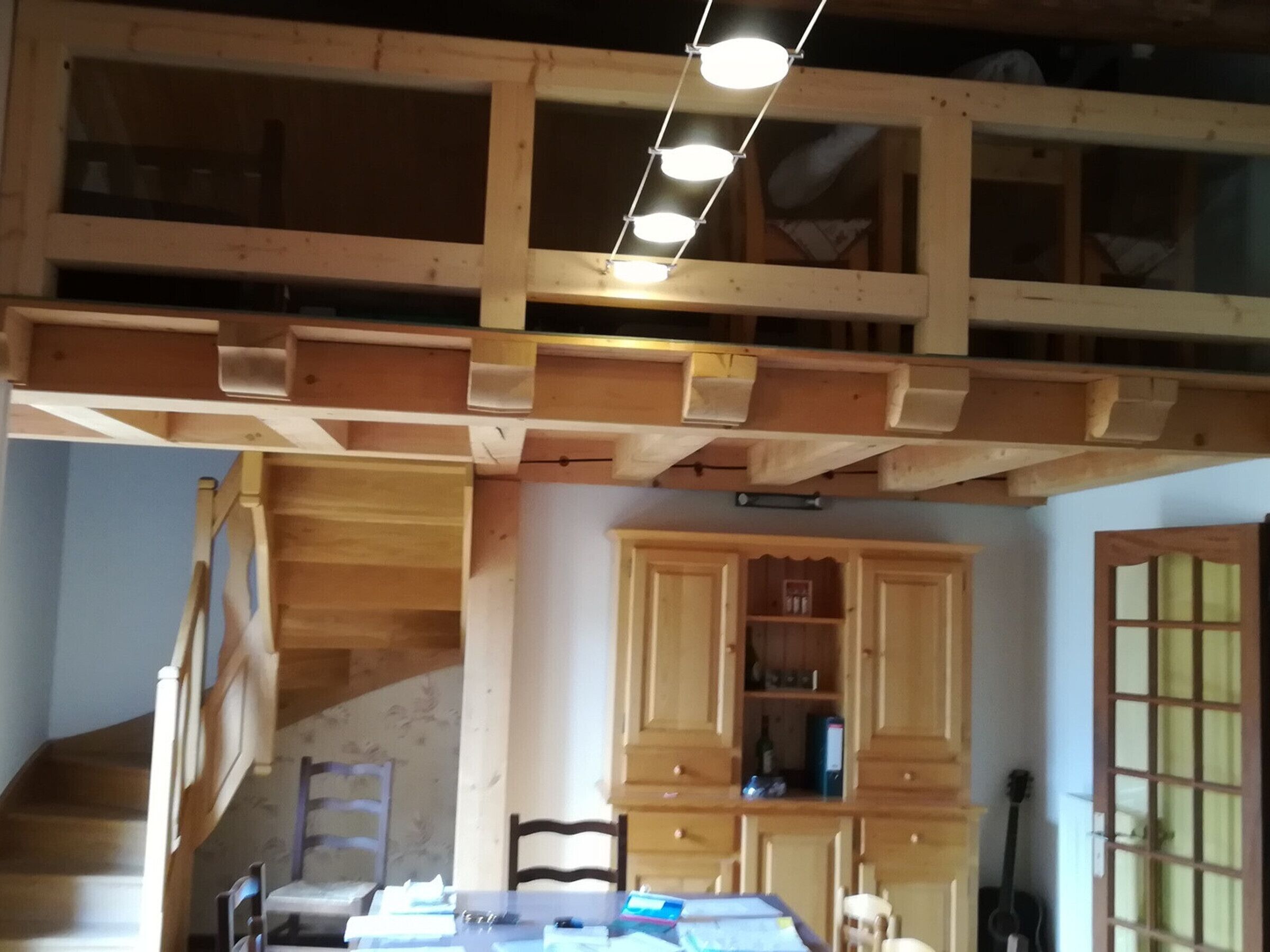 A room with a wooden ceiling structure, a dining table with chairs, and a guitar leaning against the wall.