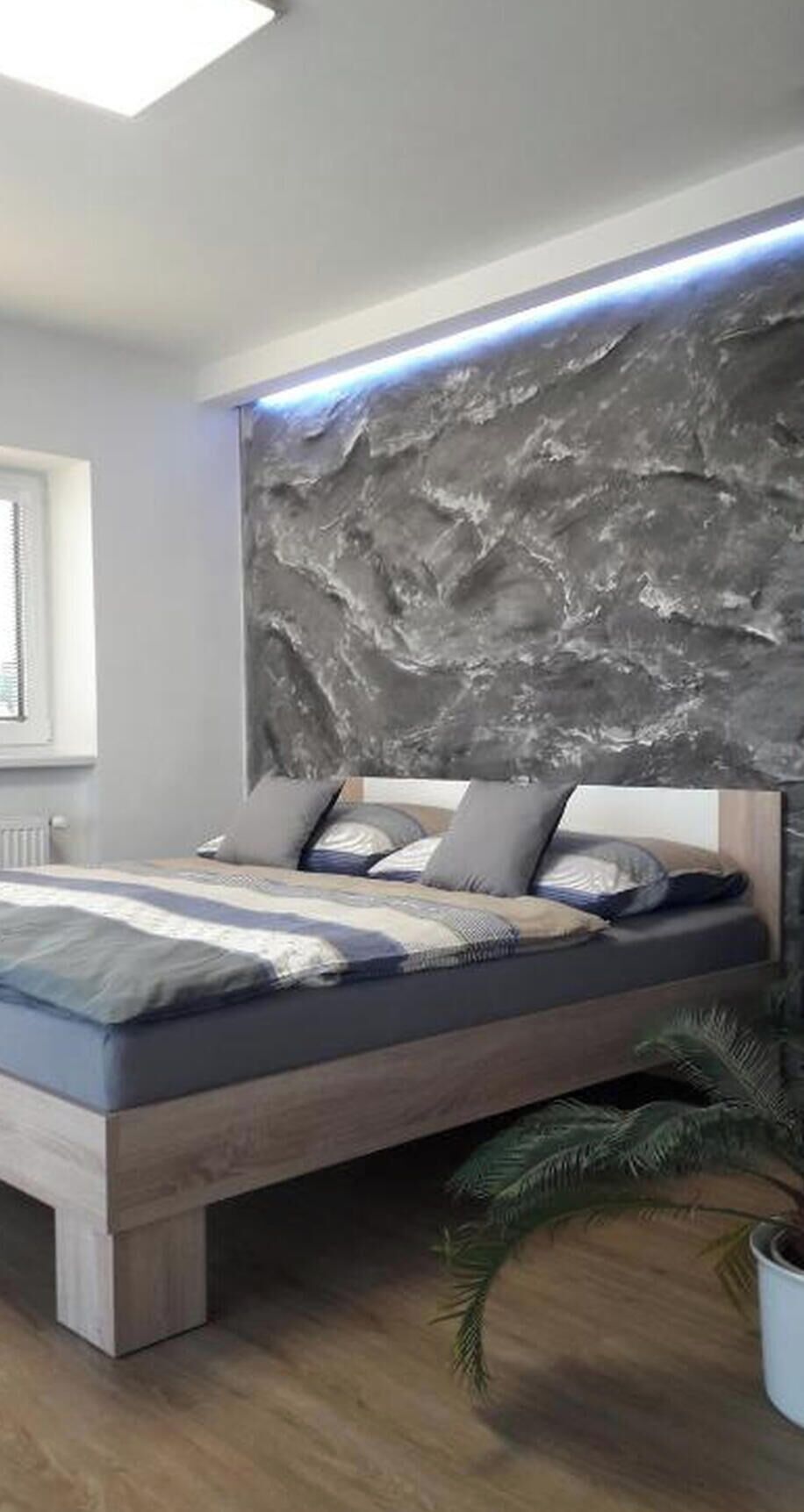 Ein modernes Schlafzimmer mit einem Bett, einer Wand mit Struktur und einem Fenster.