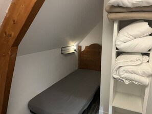Ein kleines Einzelzimmer mit Holzkopfende, einer Wandleuchte und einem Regal mit gefalteten Decken.