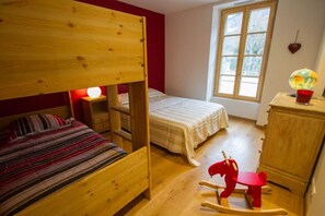 Ein Zimmer mit Etagenbett, einem Einzelbett, einem Schaukelpferd, einem kleinen Tisch mit Globus und einem Fenster mit Blick auf Bäume.