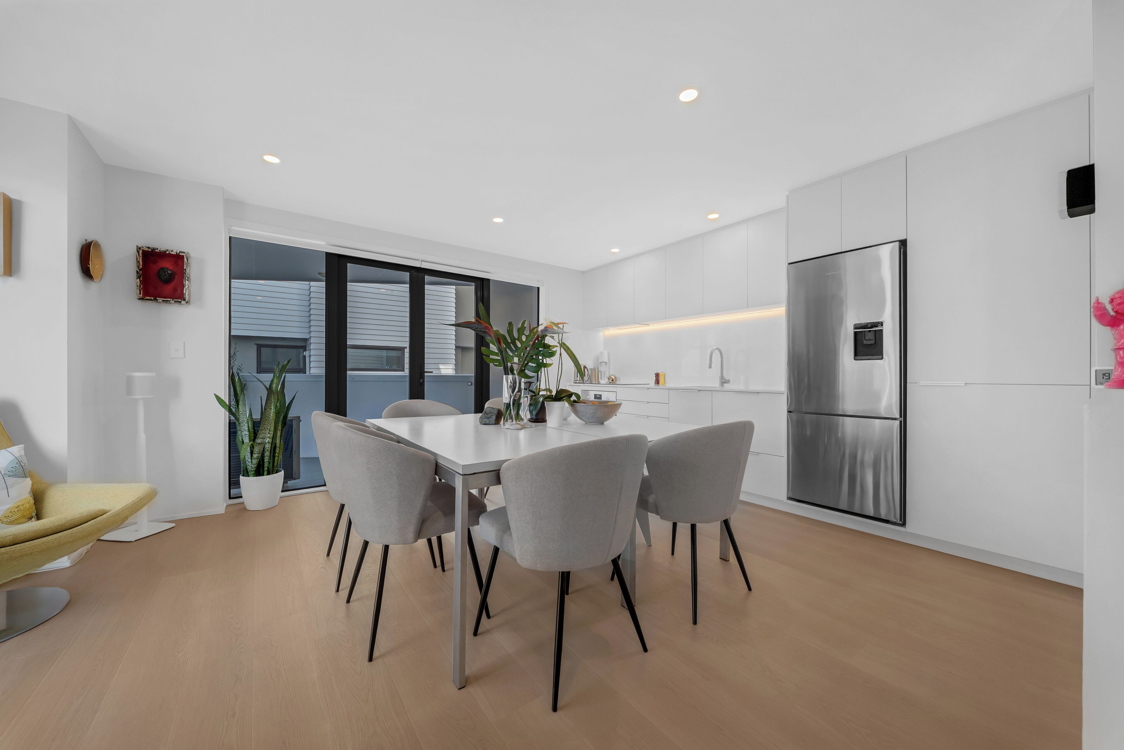Een moderne keuken met een eethoek, voorzien van een roestvrijstalen koelkast, een wit aanrecht en een eettafel met stoelen.
