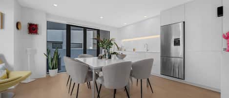 Une cuisine moderne avec un coin repas, comprenant un réfrigérateur en acier inoxydable, un plan de travail blanc et une table à manger avec des chaises.