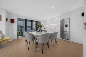 A modern kitchen with a dining area, featuring a stainless steel refrigerator, a white countertop, and a dining table with chairs. - A light-filled Ponsonby townhouse. Open-plan living opens to a sheltered balcony, with a restful queen bedroom and a separate TV lounge to retreat to. Step outside and you're spoilt for choice: Ponsonby Road's cafés, shops and restaurants. (Ponsonby)