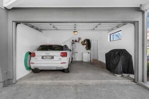 A white car parked inside a garage with a washing machine and a covered item to the right. - A light-filled Ponsonby townhouse. Open-plan living opens to a sheltered balcony, with a restful queen bedroom and a separate TV lounge to retreat to. Step outside and you're spoilt for choice: Ponsonby Road's cafés, shops and restaurants. (Ponsonby)