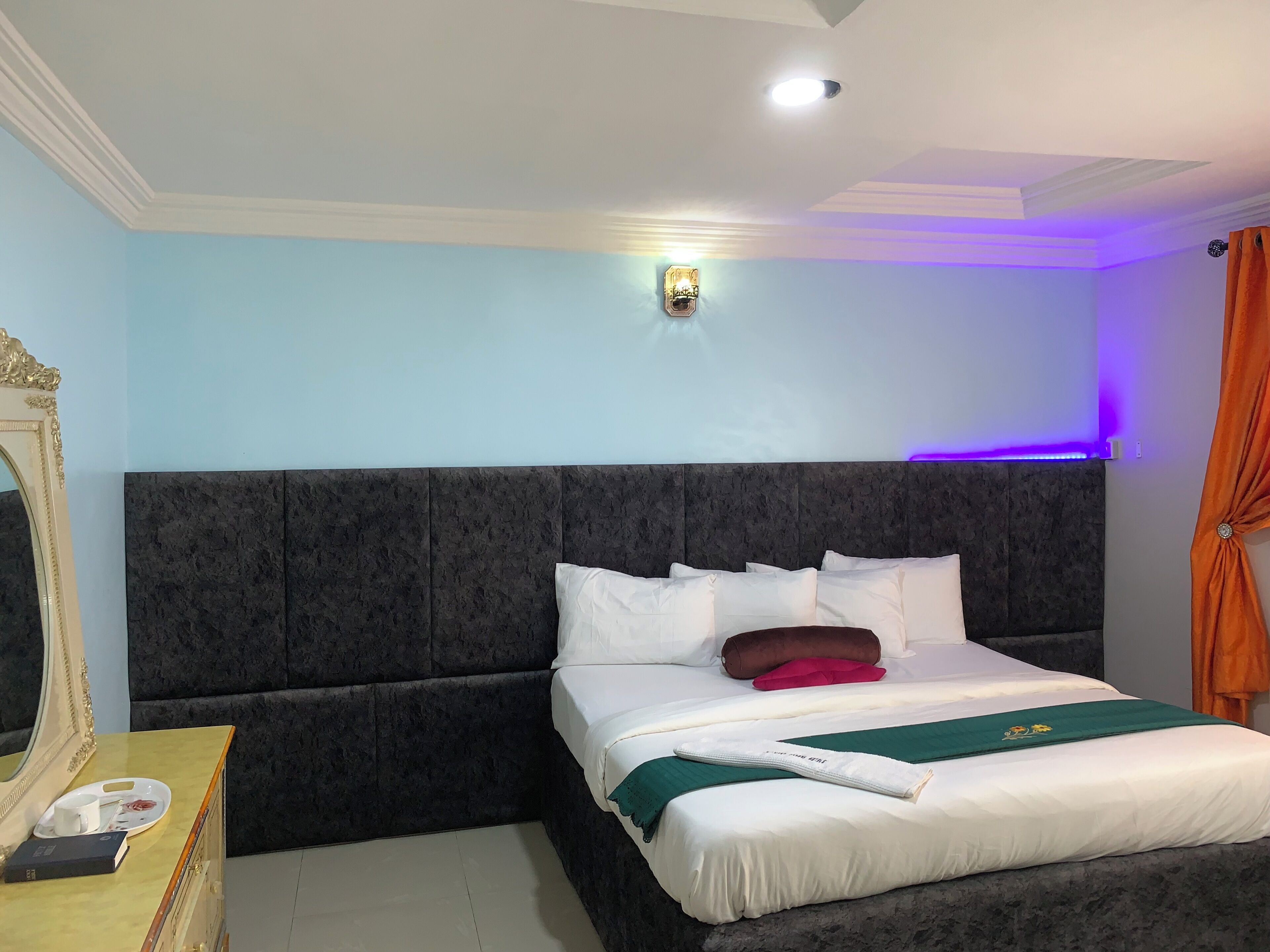 A hotel room with a large bed, a bedside table with a mirror, and a wall-mounted light fixture.