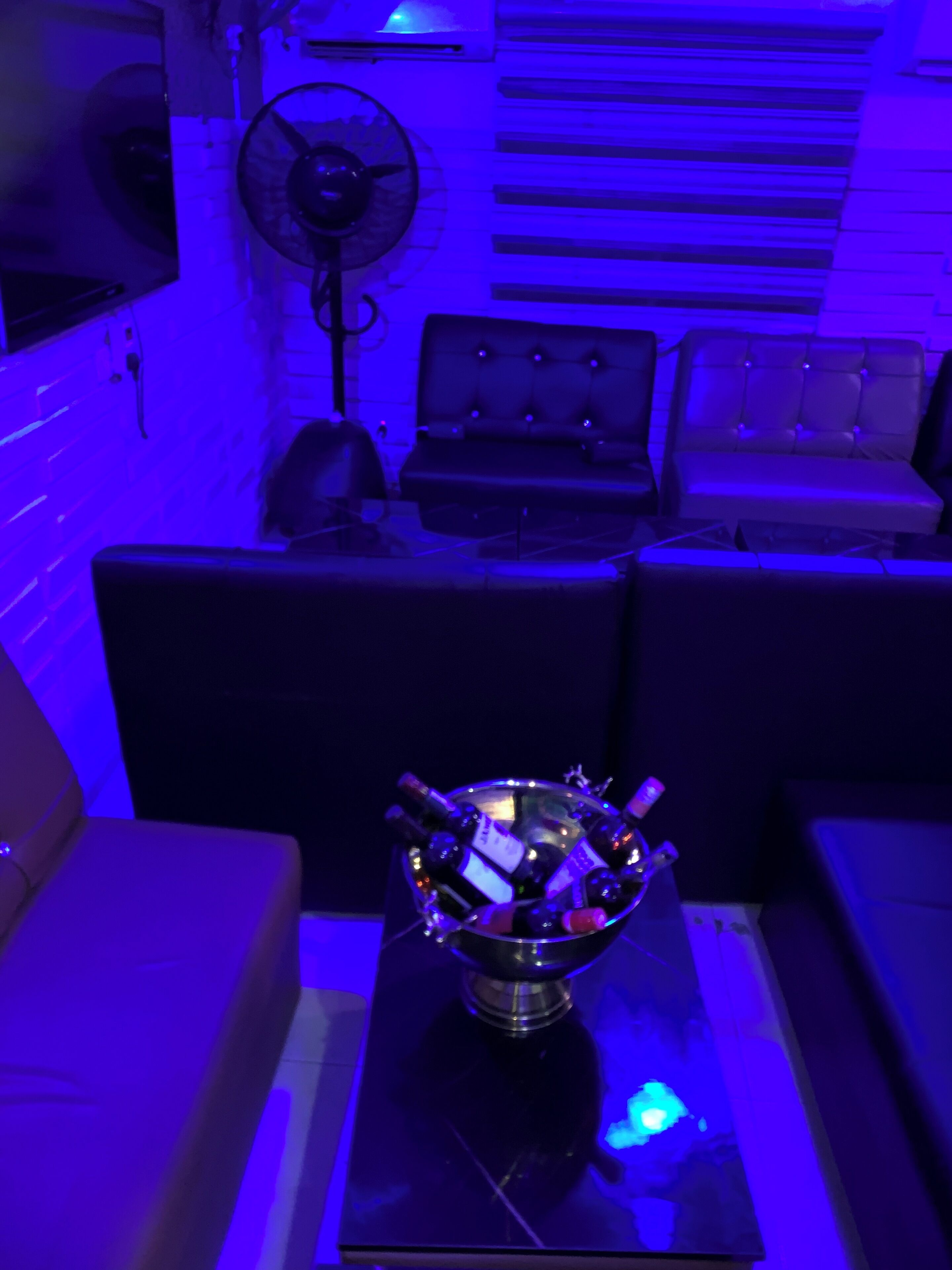 Um quarto com um sofá, uma mesa com uma tigela de vidro contendo garrafas e um ventilador.