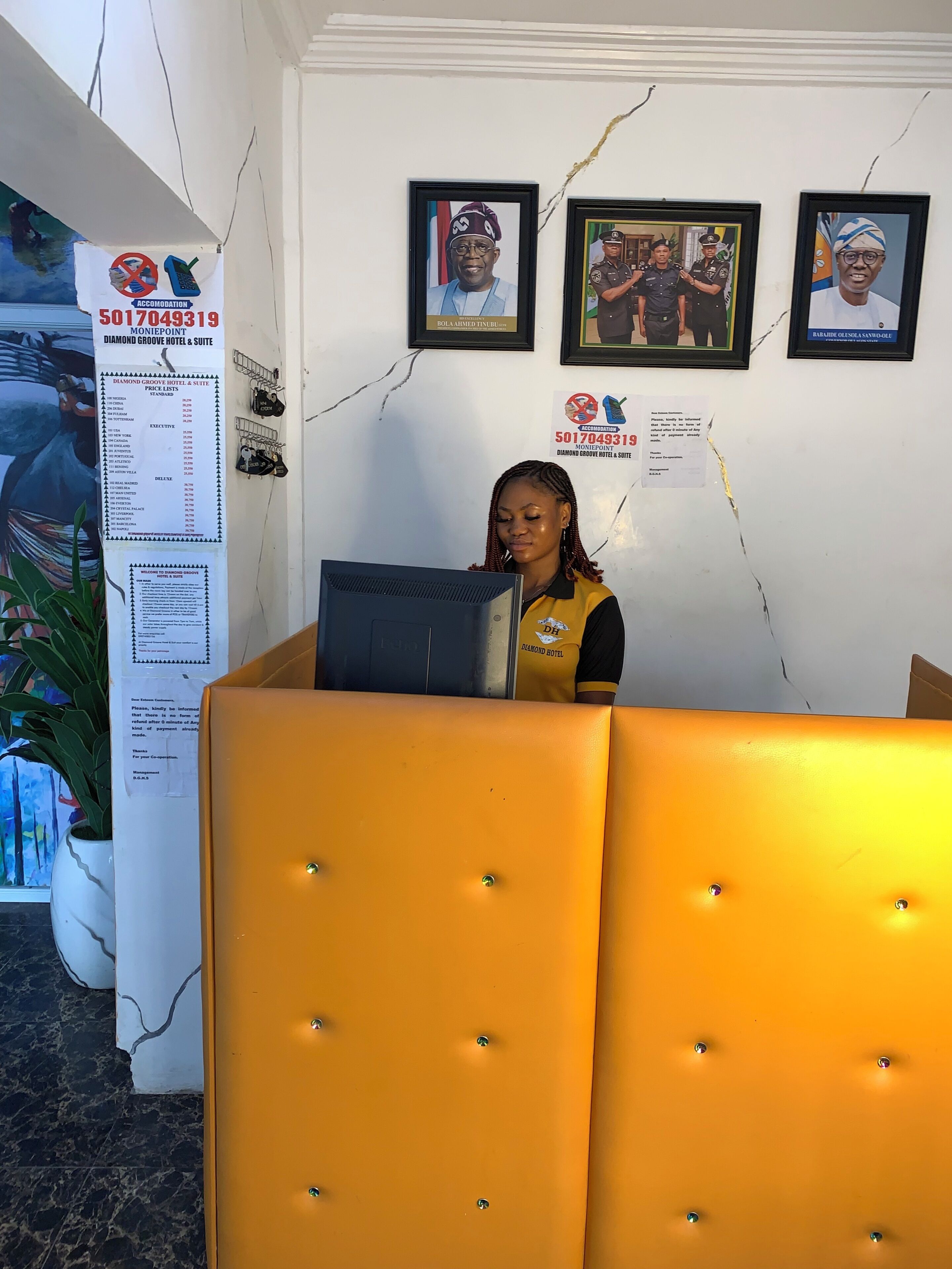 Zona de recepción con una recepcionista detrás del mostrador, cuadros en la pared y un tablón de anuncios con una lista de precios.