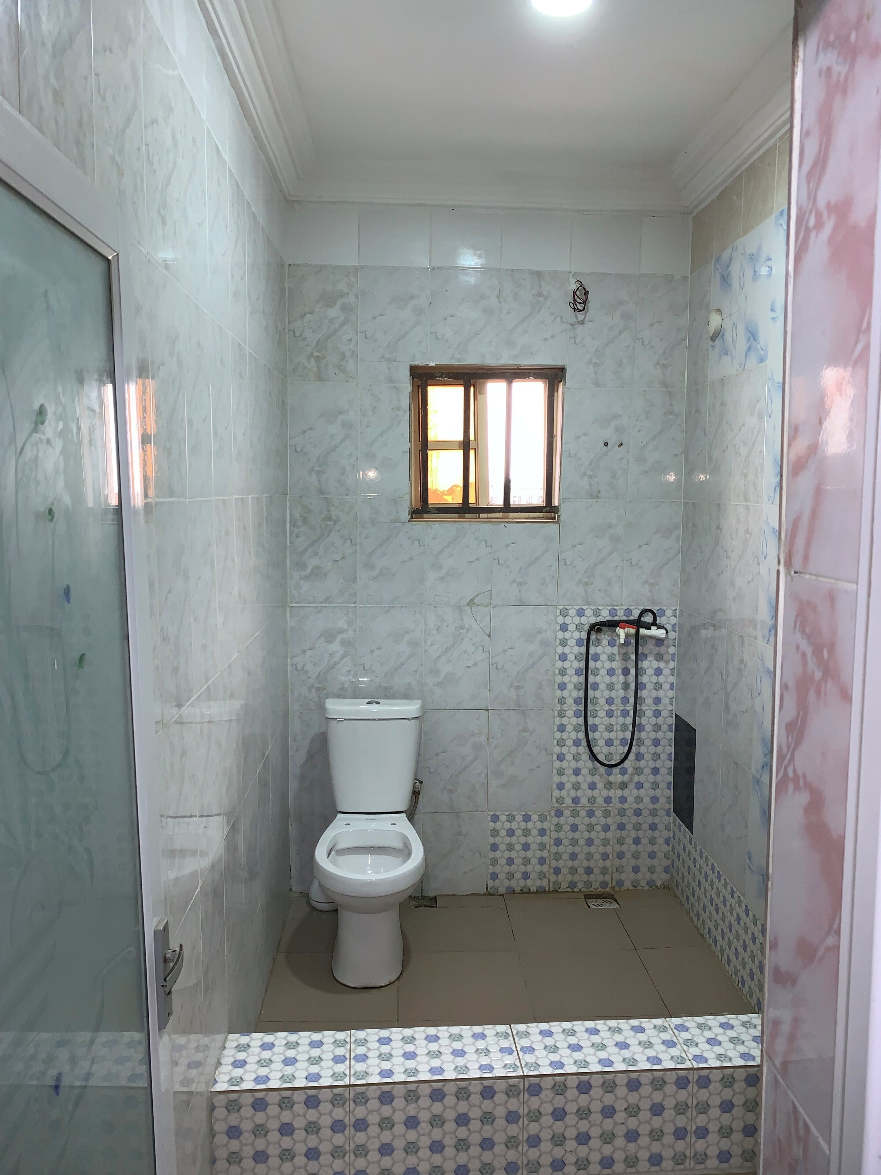 A bathroom with a toilet, a shower area, and a small window.