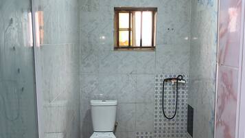 Un baño con inodoro, zona de ducha y un ventanal pequeño.