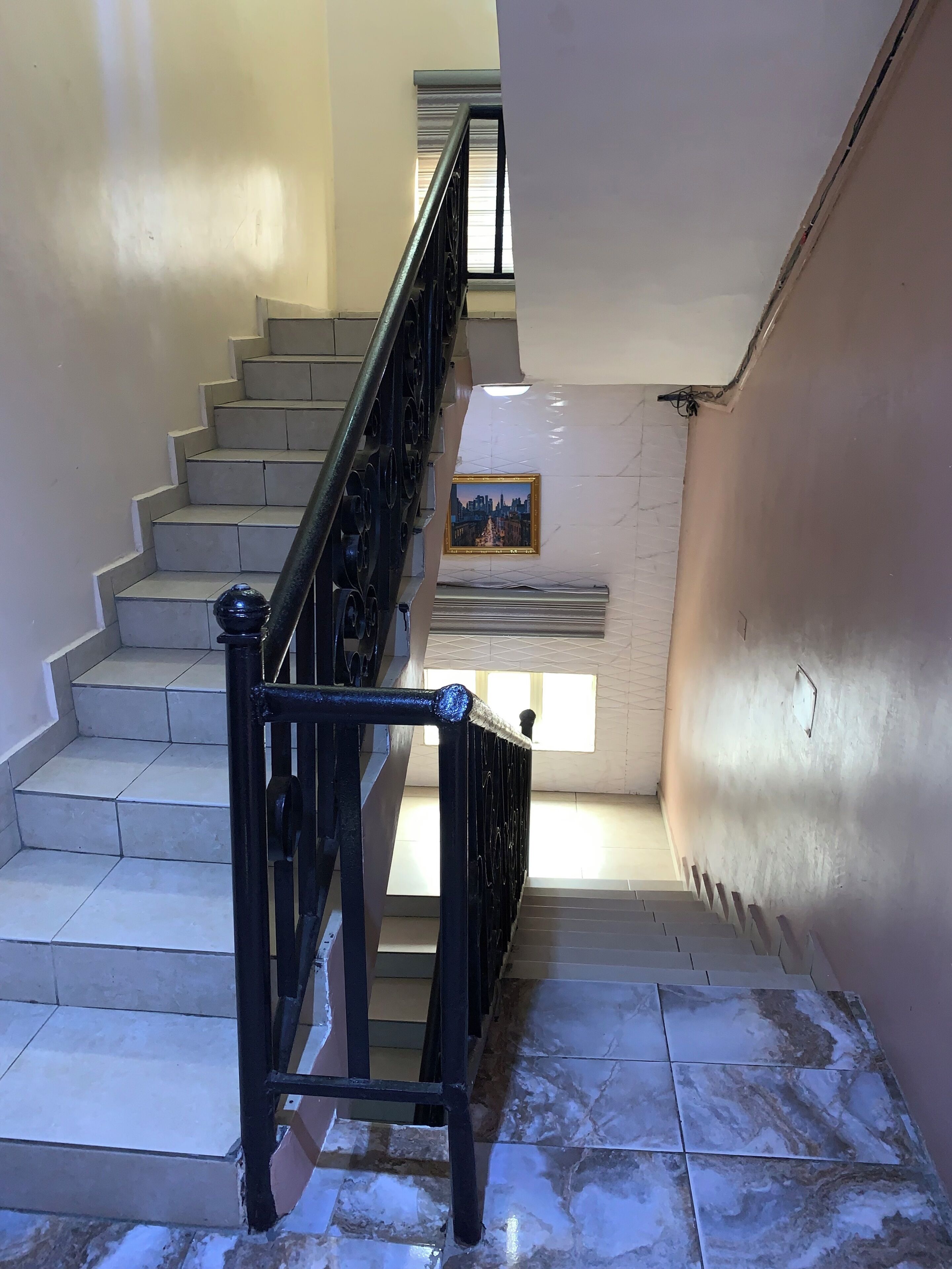 Una escalera con barandilla de metal negro, un cuadro en la pared y suelo de baldosas.
