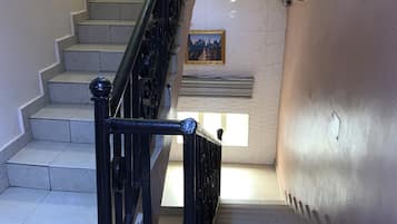 Una escalera con barandilla de metal negro, un cuadro en la pared y suelo de baldosas.