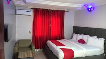 Una habitación de hotel con cama, televisión, una pequeña zona de estar y una cortina roja.