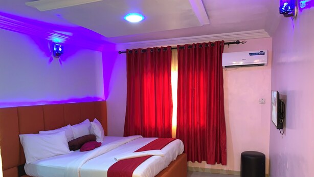 A hotel room with a bed, red curtains, an air conditioning unit, and a wall-mounted phone. - Diamond Groove Hotel & Suites (Sangotedo)