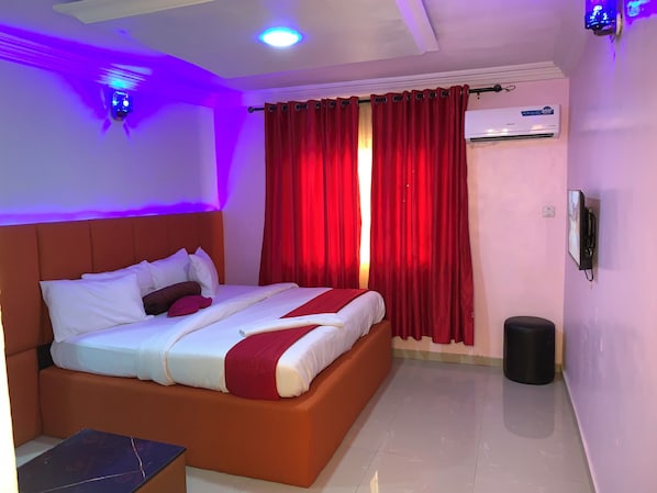 A hotel room with a bed, red curtains, an air conditioning unit, and a wall-mounted phone.