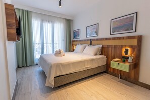 A hotel room with a bed, a bedside table with a lamp, a TV mounted on the wall, and a window with curtains.