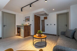 Una sala de estar moderna con sofá, una mesa de centro con una planta y una zona de cocina con fregadero y armarios.