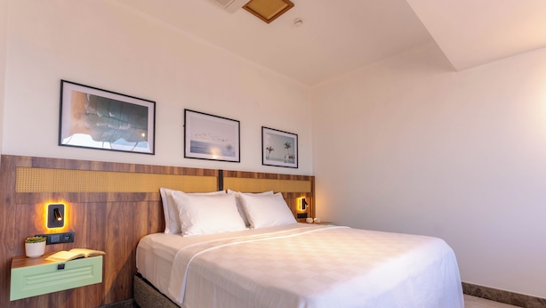 A hotel room with a large bed, a nightstand with a lamp, and three framed pictures on the wall. - ARVIA SUITES (Altinova)