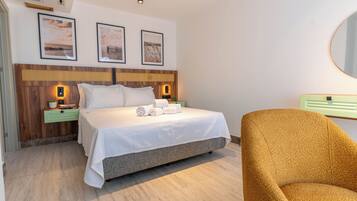 A hotel room with a bed, a nightstand, a green drawer, a round mirror, and a brown armchair.